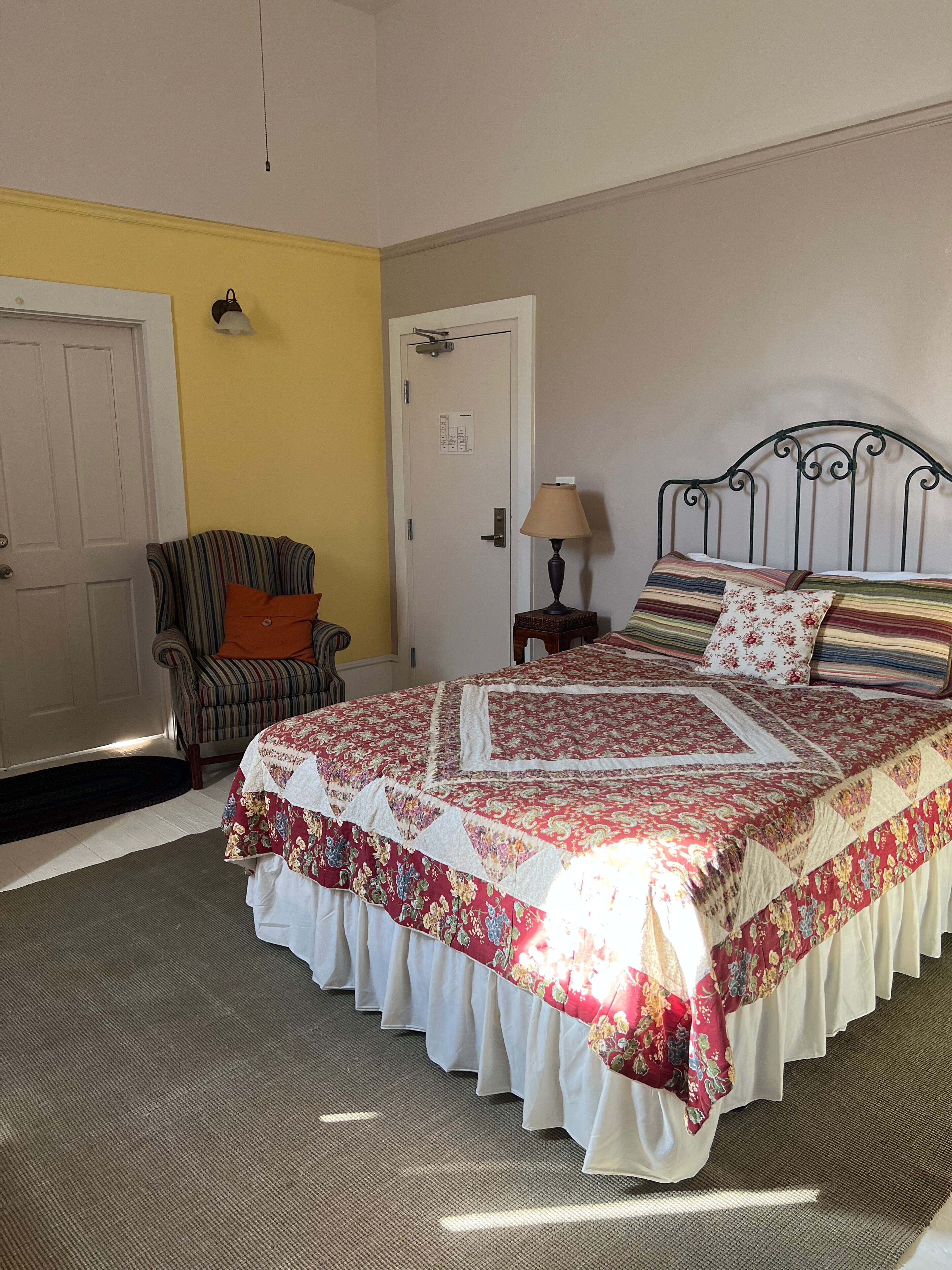 A bedroom with a bed, a chair, a lamp, and a door.