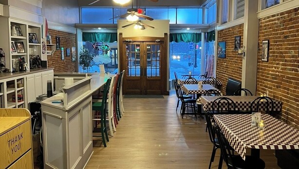 Un restaurante con zona de bar, suelo de madera, manteles a cuadros y pared de ladrillo.