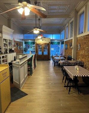 A restaurant with a bar area, wooden flooring, checkered tablecloths, and a brick wall. - The Eagles Nest Inn (Louisiana)