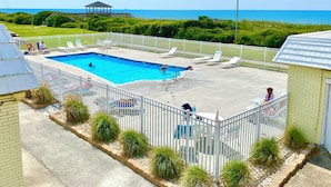 A swimming pool with a view of the ocean, surrounded by a white fence and lounge chairs. - Charming studio with Ocean View, AC, wifi, pool, on-site laundry room (Atlantic Beach)
