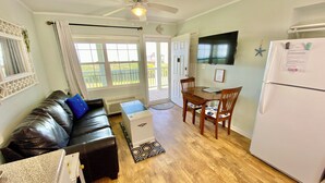 A compact living space with a sofa, a dining table with chairs, a refrigerator, and a ceiling fan. - Charming studio with Ocean View, AC, wifi, pool, on-site laundry room (Atlantic Beach)