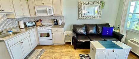 A compact living space with a kitchenette, a black leather sofa, and a small table.
