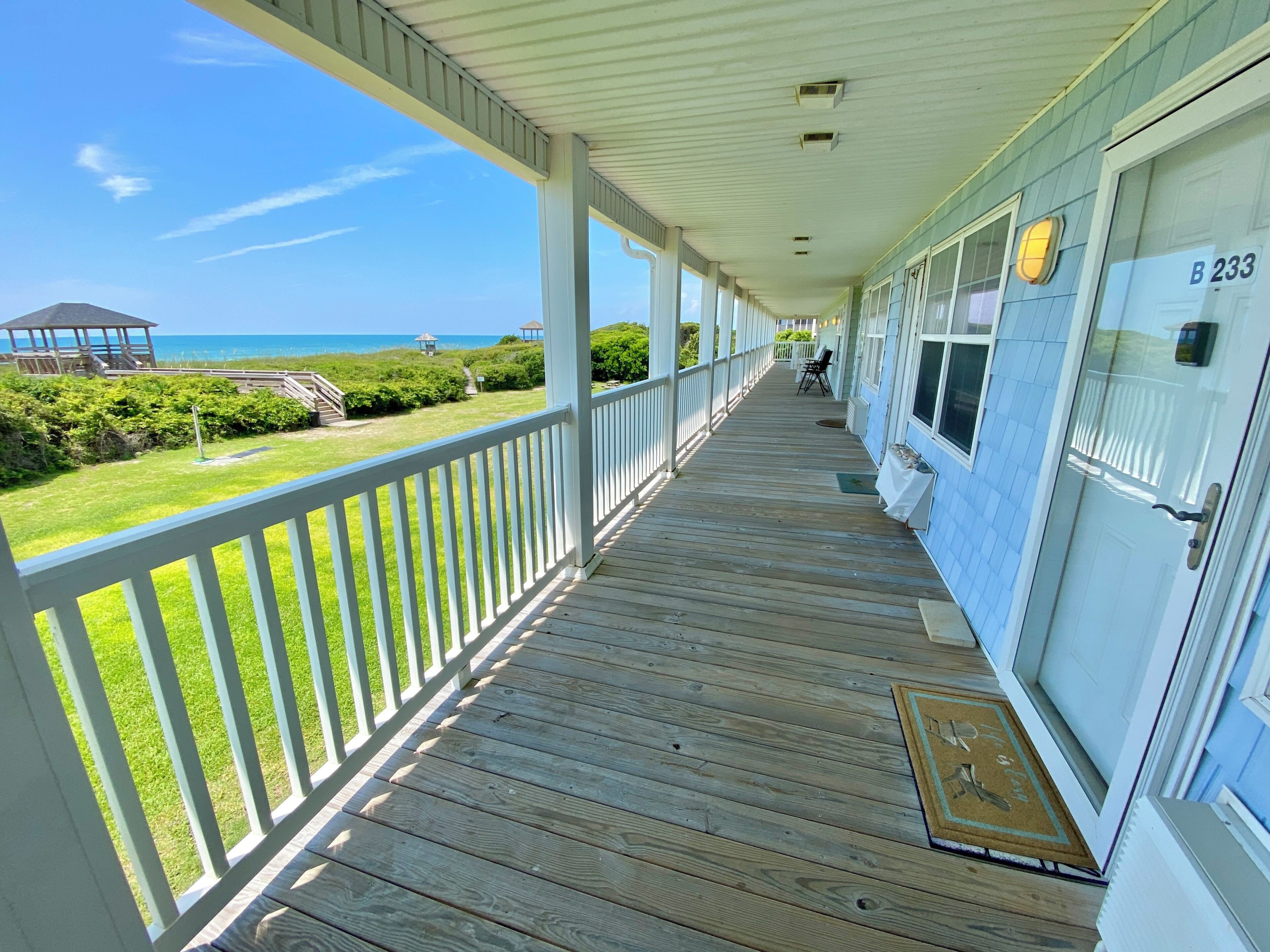 A covered porch with a view of the ocean, a door labeled B 233, and a doormat with a key.