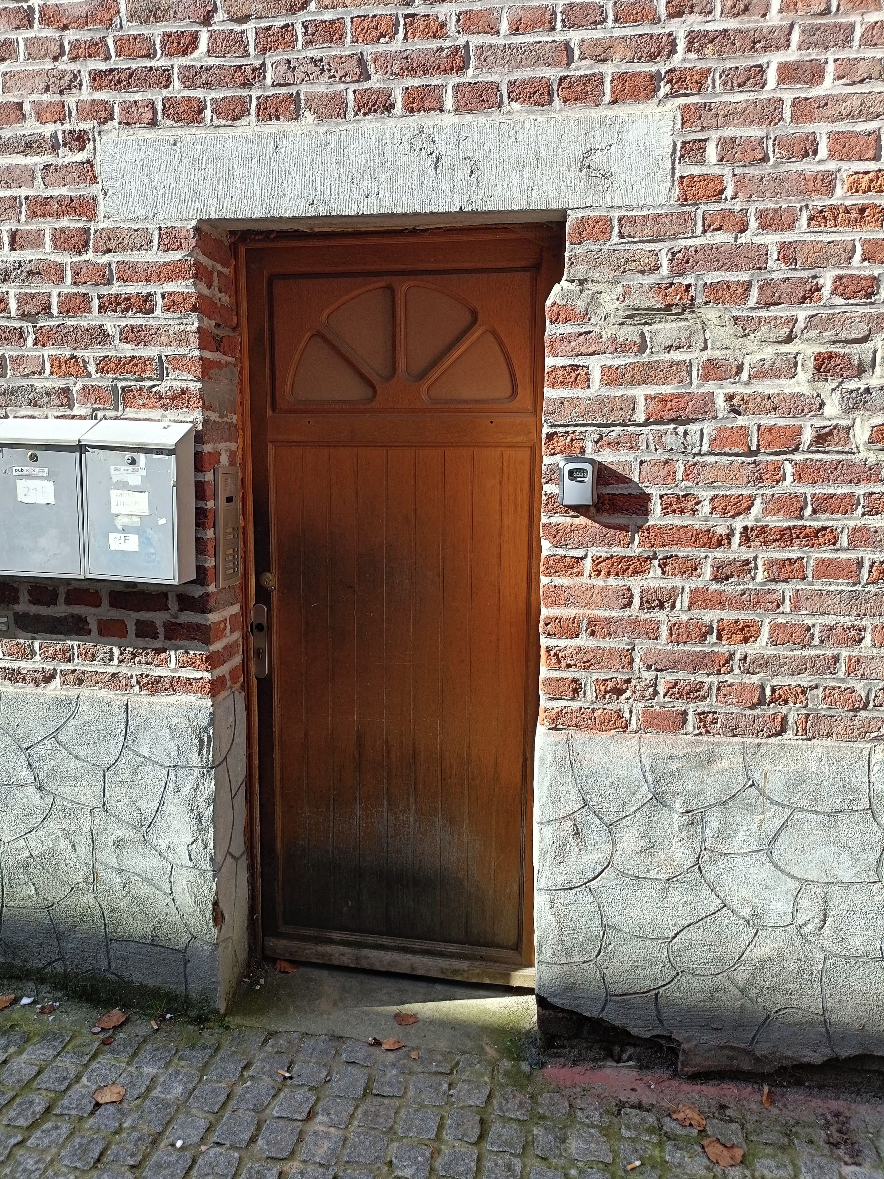 Een houten deur met een bakstenen muur, een brievenbus en een beveiligingsbox.