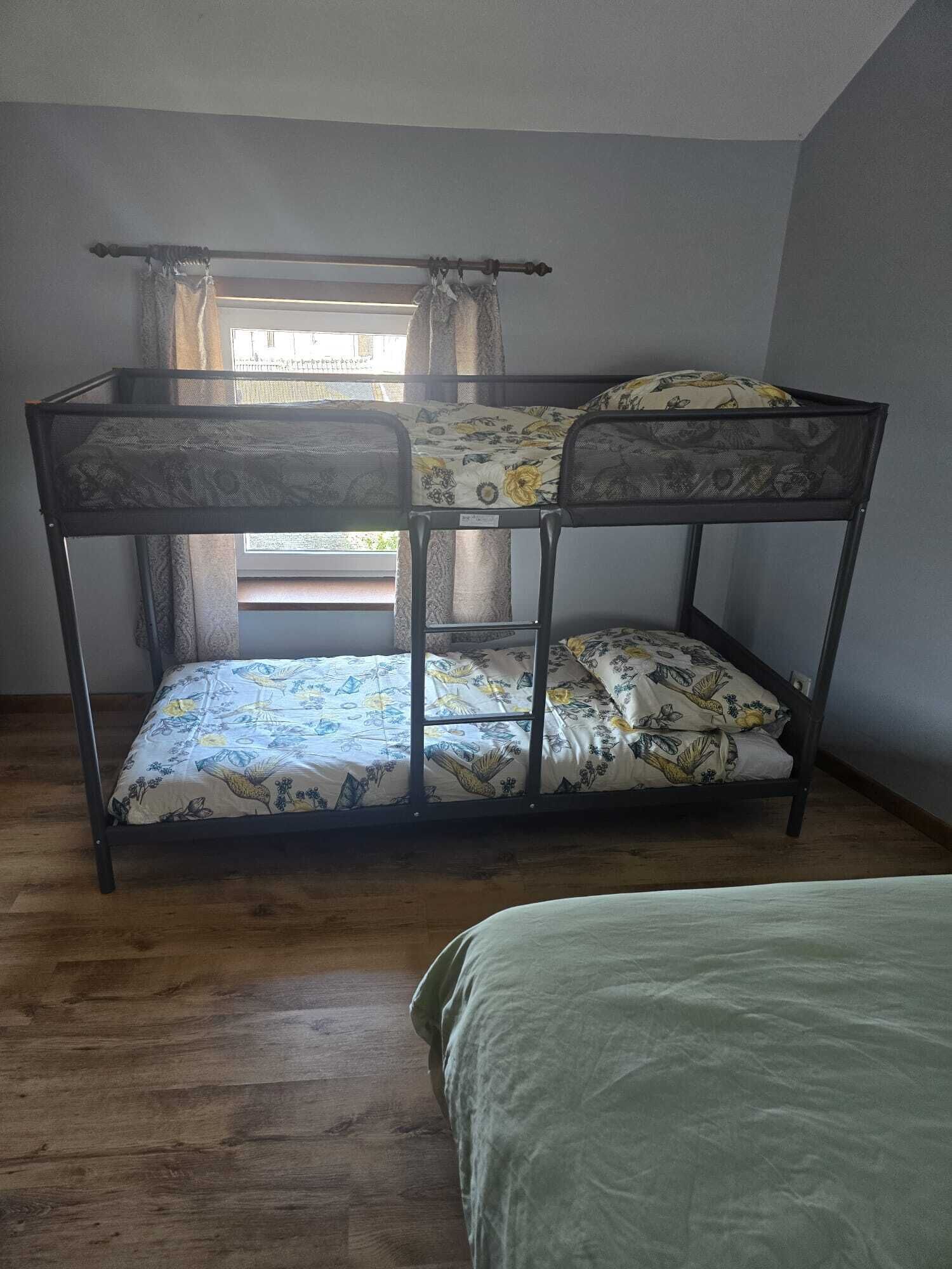 Un letto a castello con biancheria da letto a motivi floreali in una stanza con pavimento in legno e una finestra con tende.