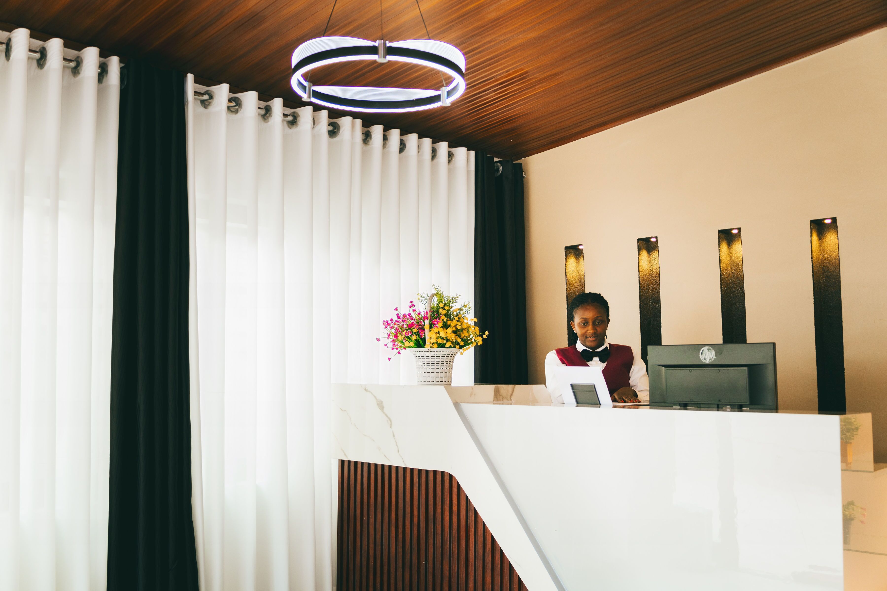 A reception desk with a modern design, a wooden ceiling, and a wall-mounted light fixture.