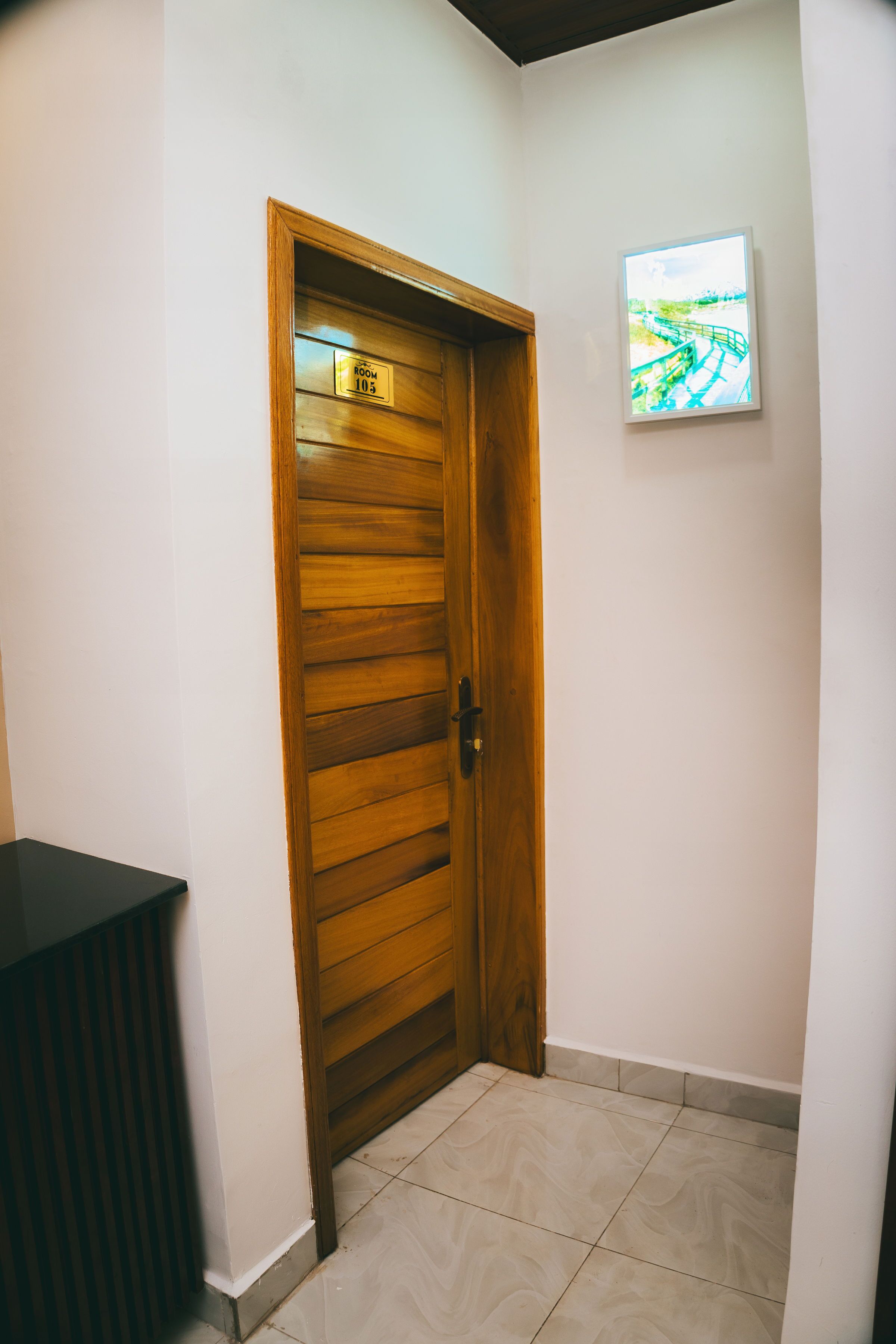 Une porte en bois avec une plaque indiquant le numéro de la chambre, un sol carrelé et un tableau encadré accroché au mur.