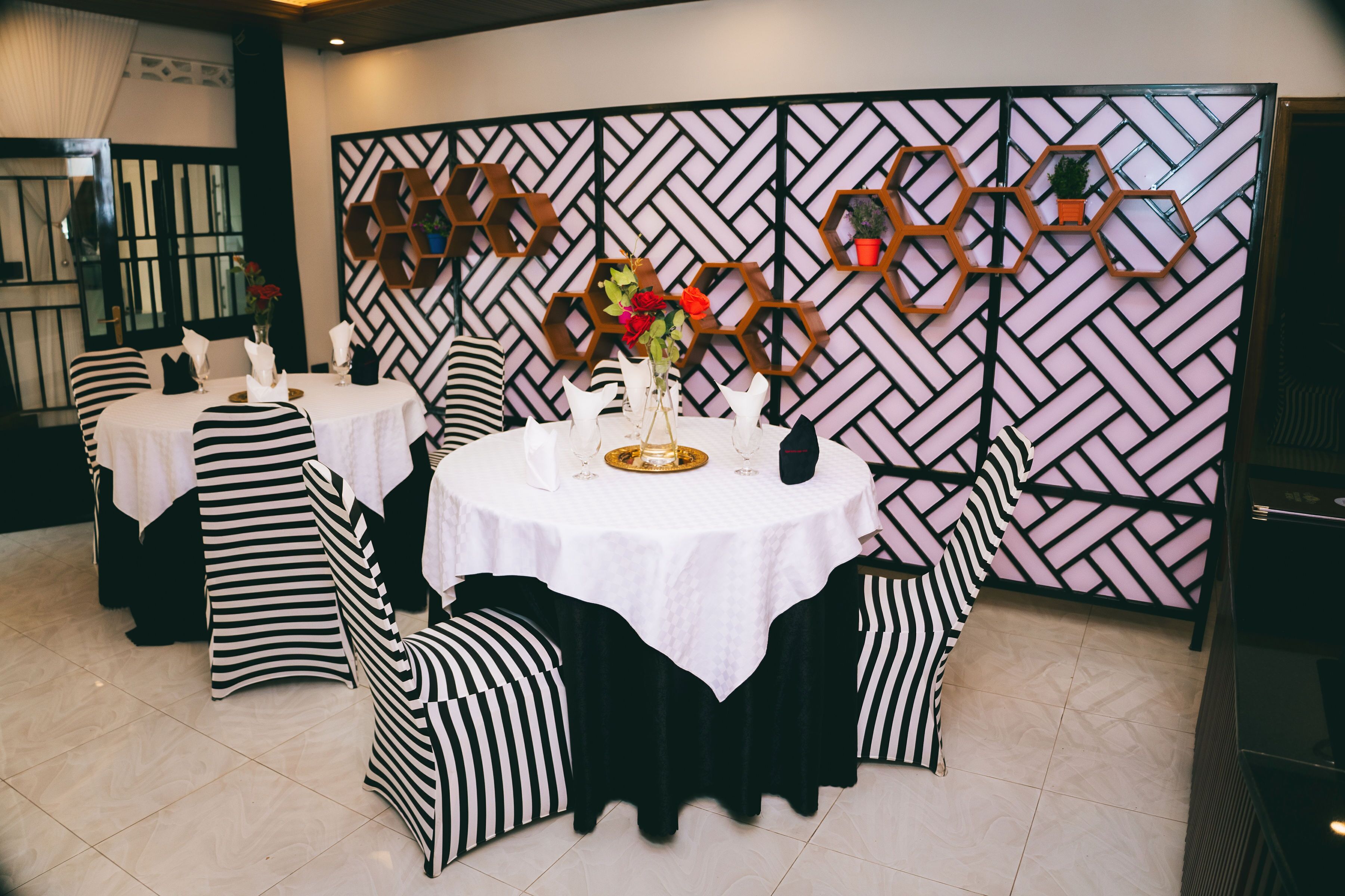 A dining area with round tables, black and white striped chairs, and a decorative wall with hexagonal patterns.