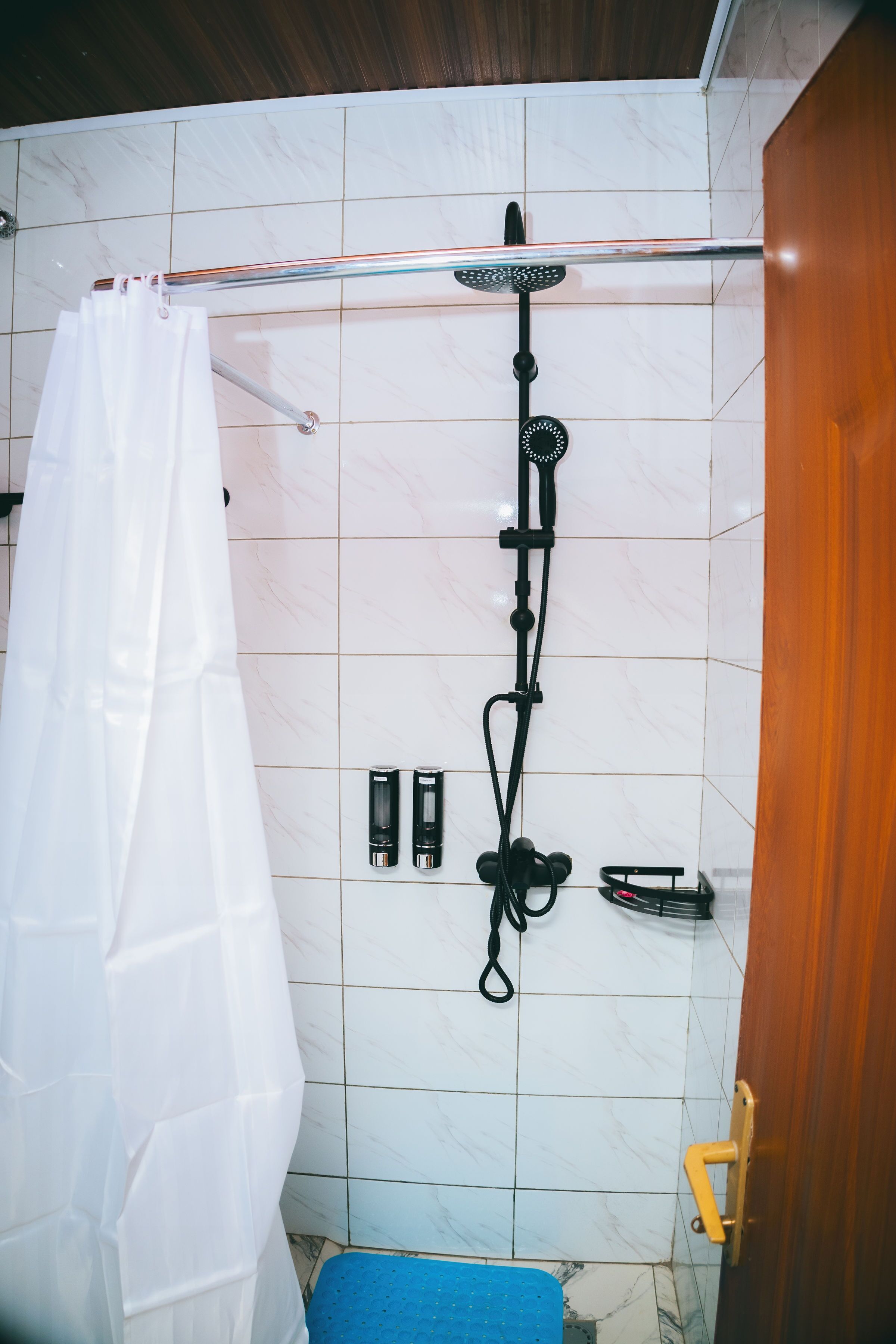 Un baño con ducha, cortina blanca y una alfombra azul.