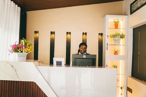 A reception desk with a marble counter, a potted plant, and a wall-mounted shelf with plants. - One Click Apartment (Kigali)