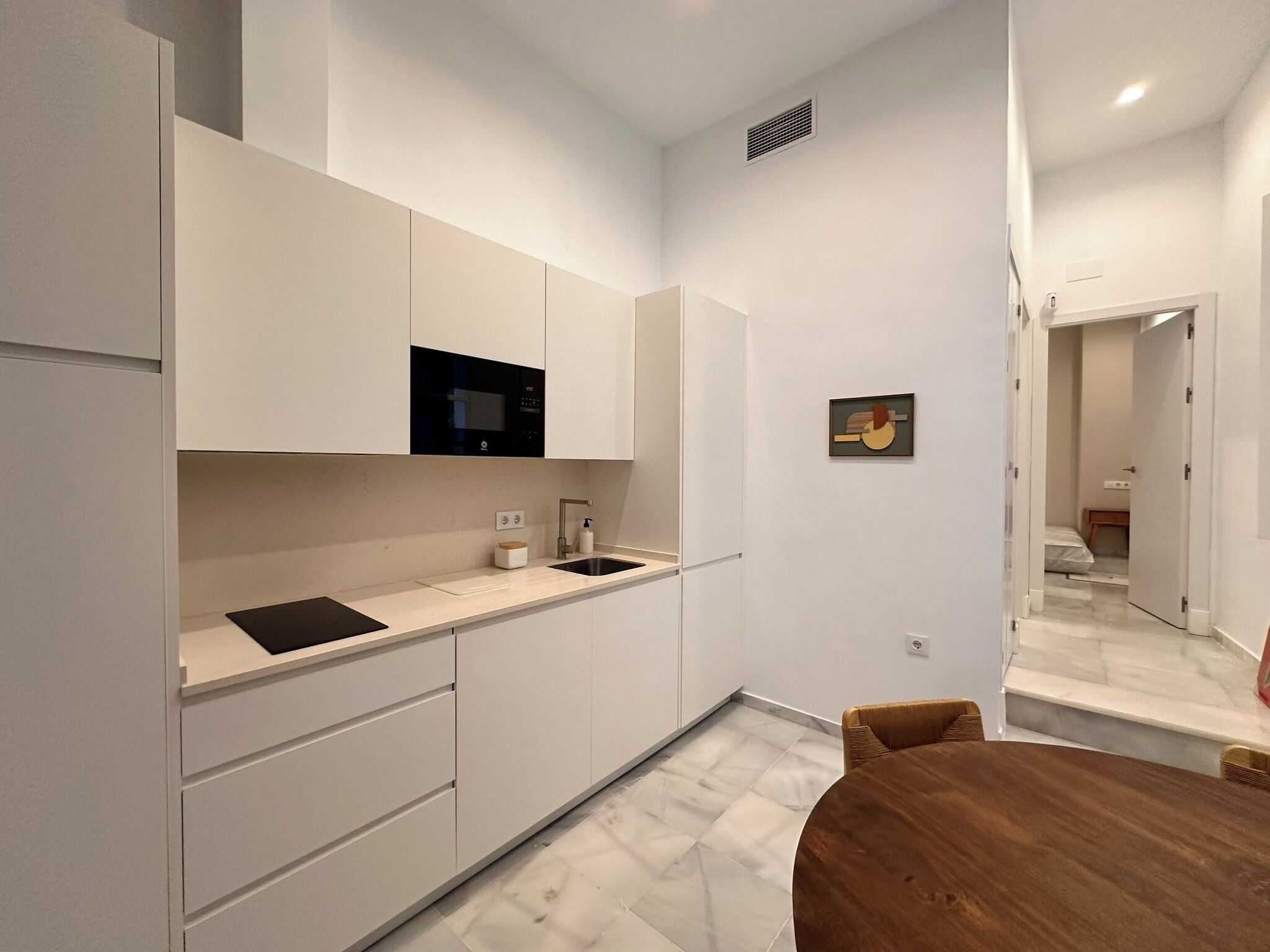 A modern kitchen with white cabinetry, a black microwave, and a wooden dining table.