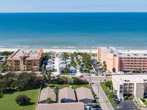 A coastal hotel with multiple buildings, a parking lot, and a view of the ocean.