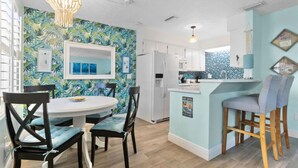 Una cocina moderna con armarios blancos, una isla azul y un diseño de pared con temática tropical.