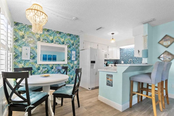 A modern kitchen with white cabinets, a blue island, and a tropical-themed wall.