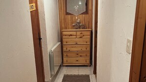 Un pasillo estrecho con un banco de madera, un pequeño aparador de madera y piso de baldosas.