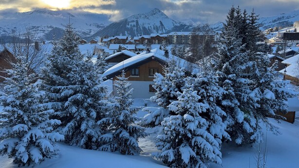 Un pueblo en la montaña cubierto de nieve con casas de madera y un albergue destacado con una cruz en el techo.