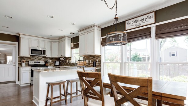 A spacious kitchen with white cabinets, a large island, wooden chairs, and a dining table. - Spacious Oasis with heated pool/spa, covered patio, office & near Lake Norman (Mooresville)