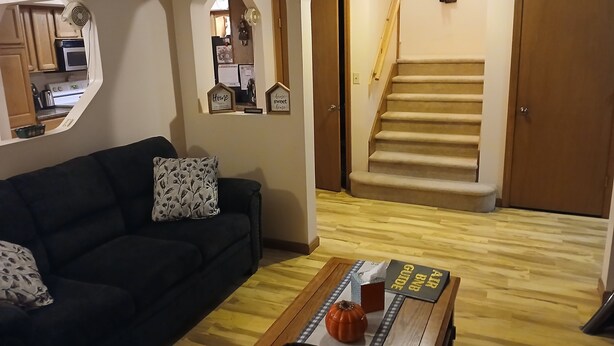 Uma sala de estar com um sofá de cor escura, uma mesa de centro de madeira com uma decoração de abóbora e uma escada que leva a uma porta.