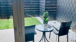 Een terras met een glazen tafel, twee stoelen, een bloempot en een zwart hek.