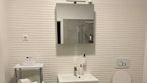Een moderne badkamer met een wit wastafelmeubel, een spiegel, een toilet en een handdoekhouder.