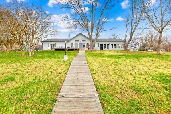 A wooden pathway leading to a house with a gabled roof and a front porch.