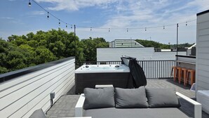 A rooftop patio with a sofa, a hot tub, and string lights.