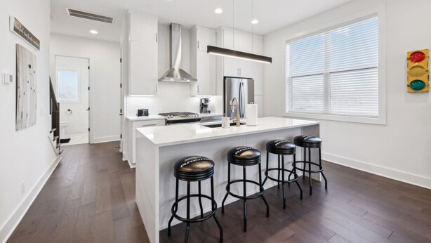 A modern kitchen with a central island, bar stools, and a large window with blinds.