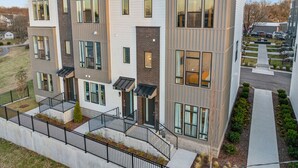 A modern multi-story residential building with a flat roof, large windows, and a covered front porch.