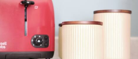 Un grille-pain rouge doté d’un cadran et d’un bouton de réglage, deux récipients beiges à parois striées et un plan de travail de couleur claire.