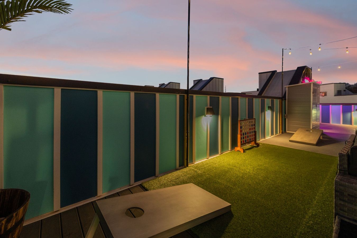 Terraço no telhado com grama sintética verde, área de estar com mesa e uma estrutura iluminada por neon.