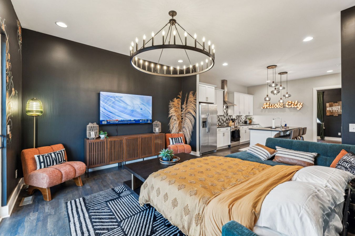 A modern bedroom with a large bed, a TV, a kitchen area, and a bar.