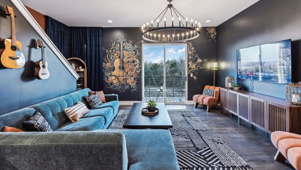 A modern living room with a blue sofa, a coffee table, and a large window with a view. - Hot Tub in Downtown! Stunning Design & Features (Nashville)