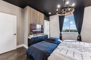 A modern bedroom with a bed, a TV mounted on the wall, and a window with curtains.