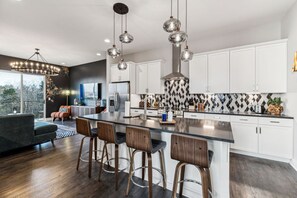 Een moderne keuken met een groot eiland, barstoelen, hanglampen en uitzicht op de buitenruimte.