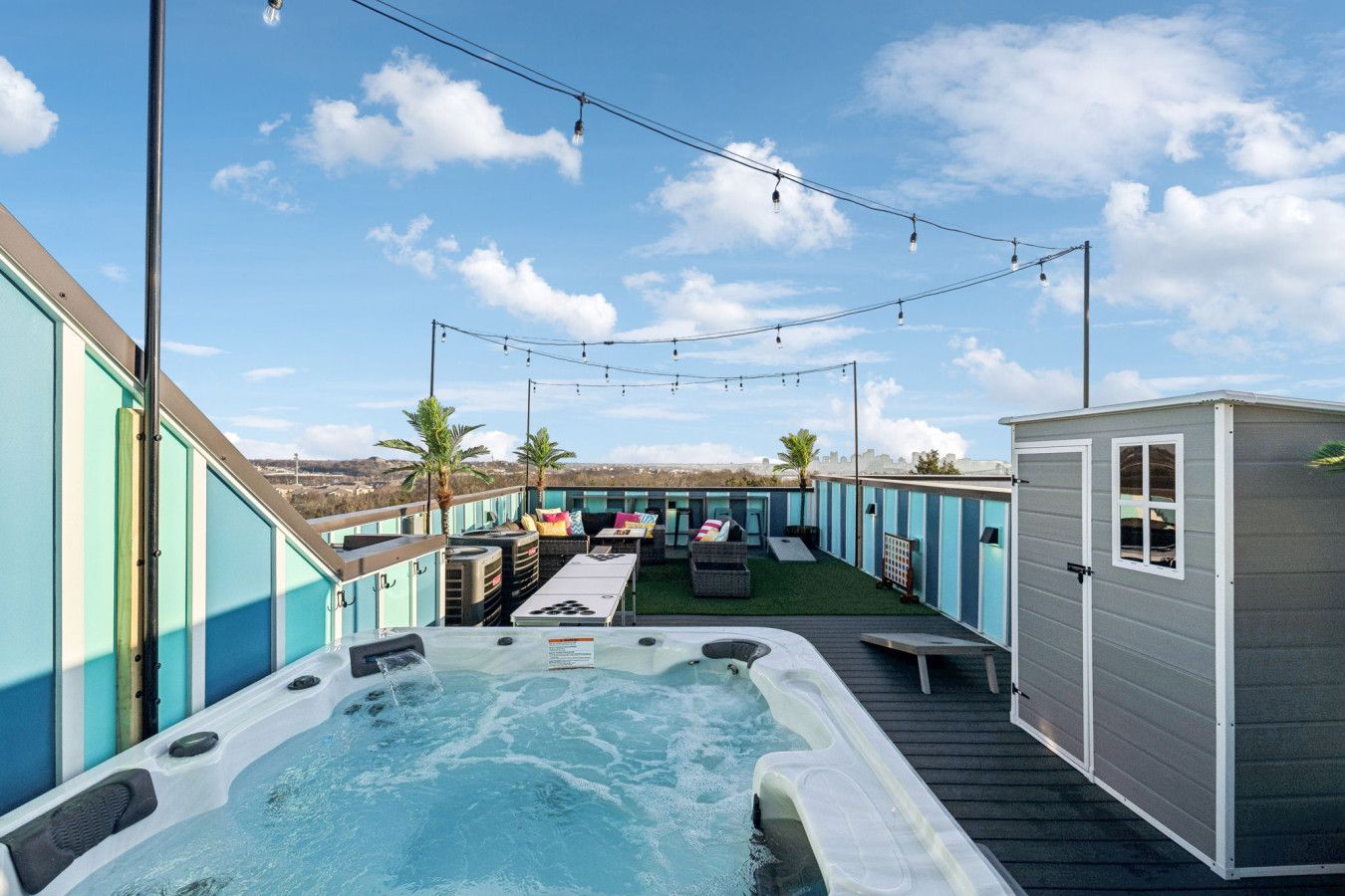 Un patio en la azotea con jacuzzi, mobiliario exterior e iluminación colgante.