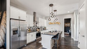 A modern kitchen with a central island, stainless steel appliances, and a neon sign reading "Music City". - Hot Tub in Downtown! Stunning Design & Features (Nashville)