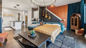 A modern living room with a sofa, a coffee table, and a chandelier. There is a staircase leading to a kitchen area. - Hot Tub in Downtown! Stunning Design & Features (Nashville)