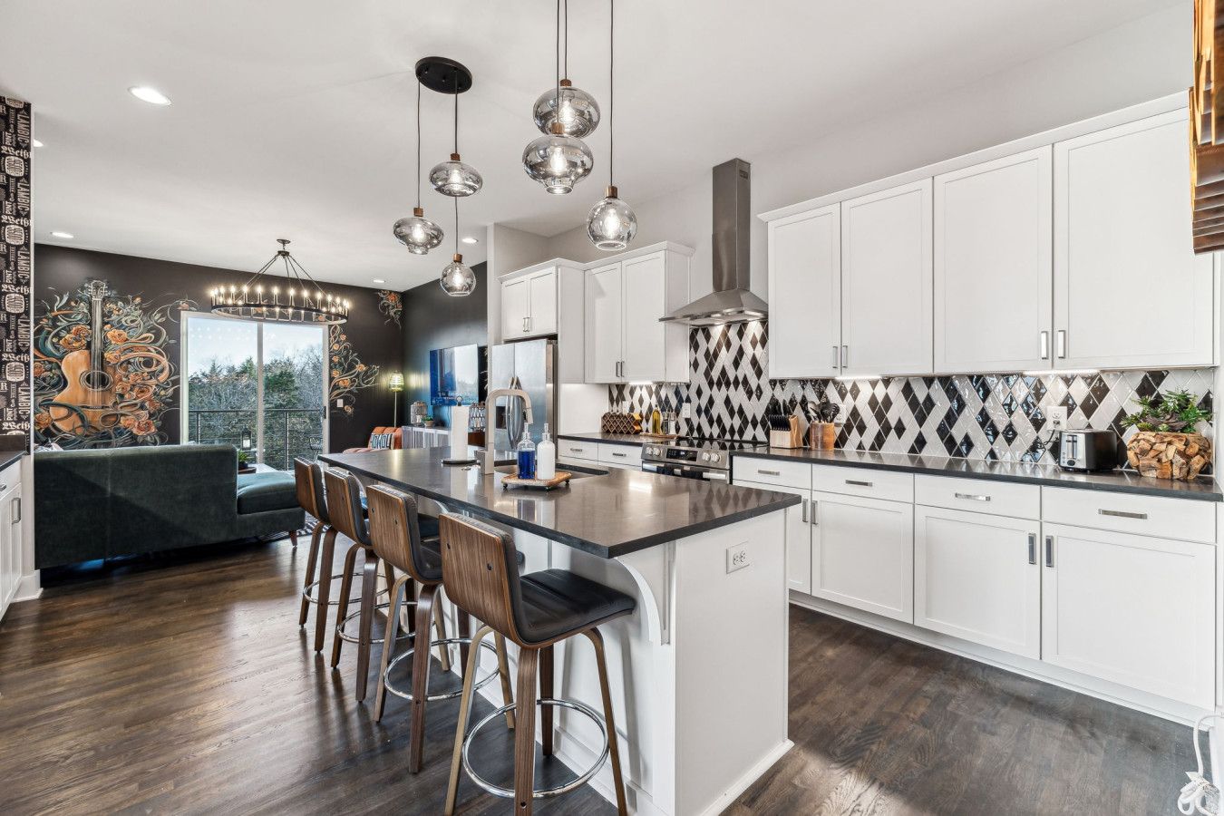 A modern kitchen with white cabinets, a large island with bar stools, pendant lighting, and a decorative backsplash.