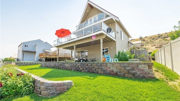 Una casa de dos pisos con un balcón, un porche cubierto y un muro de contención de piedra.
