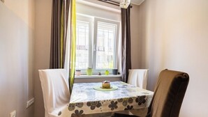 A dining area with a table covered in a floral tablecloth, two chairs, and a window with curtains. - Chic apartment -Dorcol city center with parking (Beograd)