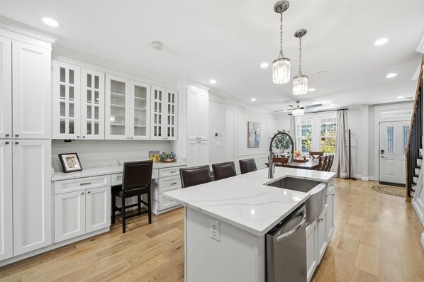 Una cocina moderna con armarios blancos, una isla grande con pileta y una zona de comedor con sillas.