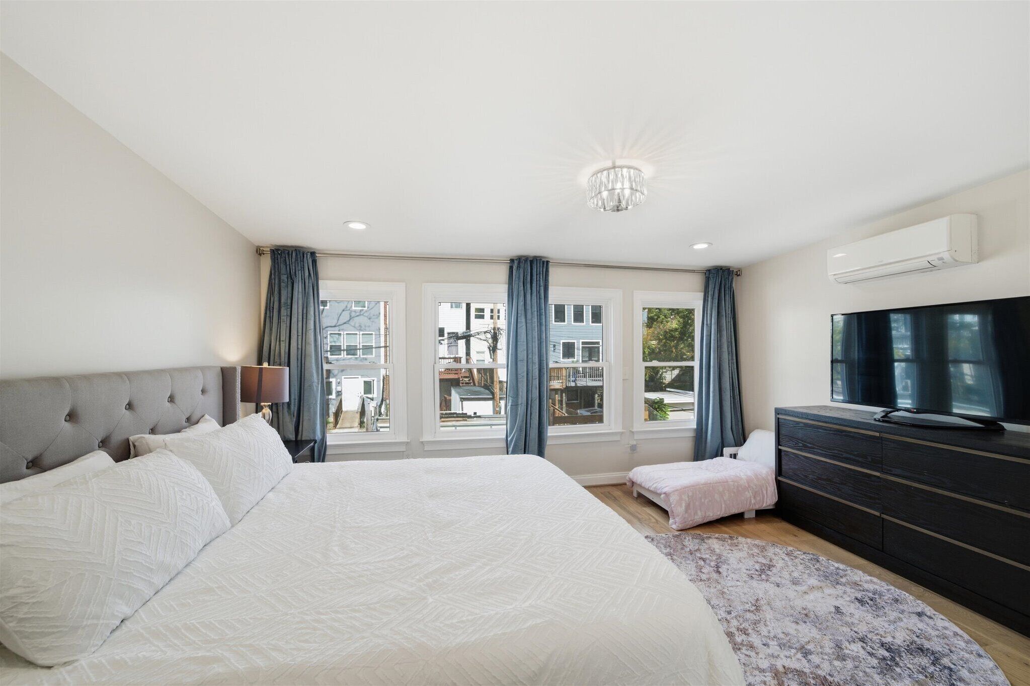 A bedroom with a large bed, a dresser, a TV, and a balcony with curtains.