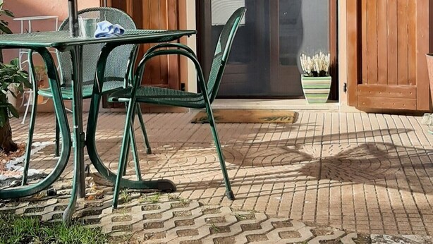 A patio area with a table and chairs, a wooden door with glass panels, and a hanging decorative item. - La Civetta, elegant one-bedroom apartment with garden, private parking 10min from the city (NAVE)