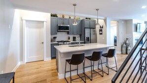 Una cocina moderna con gabinetes grises, electrodomésticos de acero inoxidable y una isla central con taburetes de bar.