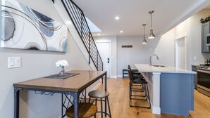 Una cocina moderna con una isla central, taburetes de bar, una escalera e iluminación colgante.