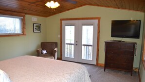 A bedroom with a bed, a chair, a dresser, a television, and a door leading to a balcony. - Locust Flats - PET-FRIENDLY MOUNTAIN Cabin = Decks-Views-Firepit (Franklin)