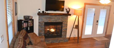 Una sala de estar con chimenea, televisor montado encima, sofá con cojines estampados y estantería.