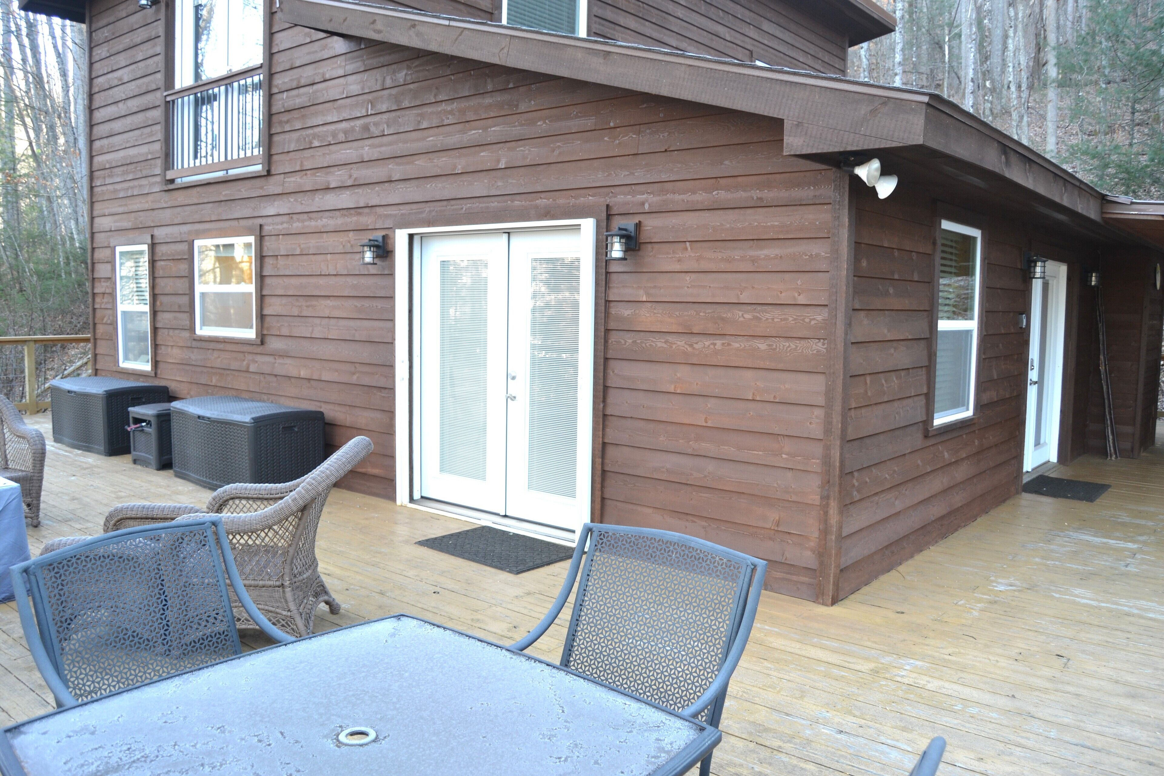 Eine Holzterrasse mit Gartenmöbeln, darunter ein Tisch und Stühle, sowie eine Schiebetür.