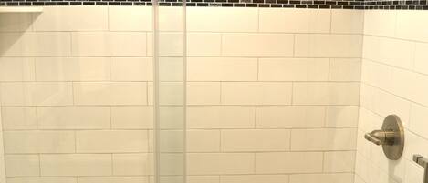 Une douche fermée par des parois en verre, avec des carreaux blancs et une bordure en mosaïque noire.