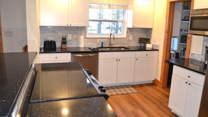 A modern kitchen with white cabinets, a black countertop, a built-in stove, and a window above the sink. - Locust Flats - PET-FRIENDLY MOUNTAIN Cabin = Decks-Views-Firepit (Franklin)